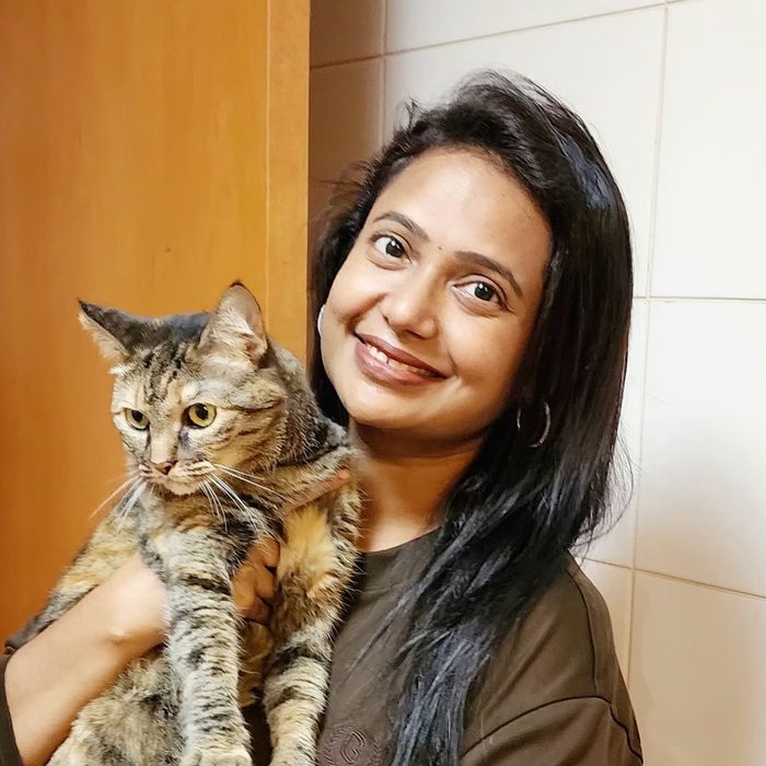 Sangeetha smiling while holding a tabby cat